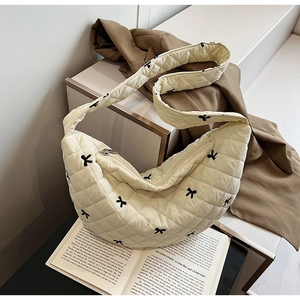 Detail of cream quilted crossbody bag with black bow embroidery and wide shoulder strap