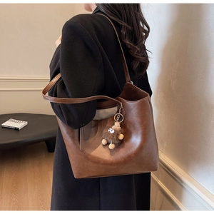 Brown soft leather tote bag with plush charm shown worn over shoulder by a model