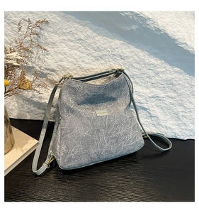Detail view of light grey handbag with marble texture and metal logo on a minimalist desk