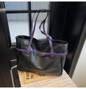 Detail view of black leather tote bag with contrasting purple handles and metallic buckle