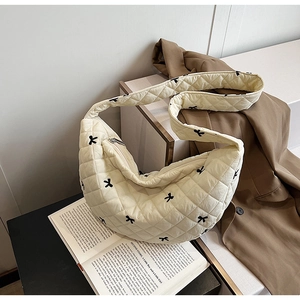 Close-up of cream quilted crescent bag with black bow embroidery on a brown blazer