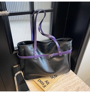Detail of black textured leather tote bag with purple straps and silver metal buckle
