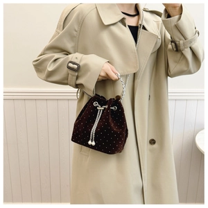 Close-up of velvet bucket bag with pearl dots and drawstring details on a trench coat