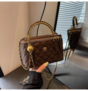 Detailansicht einer dunkelbraunen Stepptasche mit goldener Blume und Kettenriemen