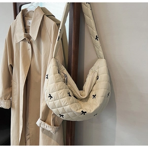 Detailed close-up of quilted cream crossbody bag with black bow embroidery and metal zipper