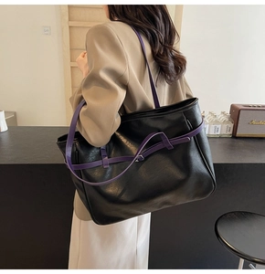 Detail of minimalist black tote bag with purple contrast strap and silver buckle accent