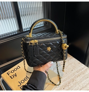 Detail der schwarzen Stepptasche mit goldener Blume und gebogenem Metallgriff