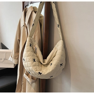 Close-up of beige quilted crossbody bag featuring elegant black bow embroidery details