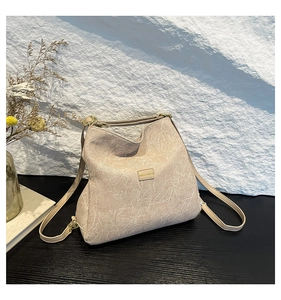 Detailed close-up of beige cracked texture faux leather bag with golden metal logo
