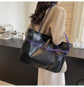 Detail of a large black tote bag with purple straps and polished leather texture