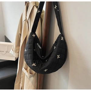 Detail of black quilted crescent bag with white bow embroidery and metallic zipper