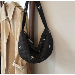 Detail of black quilted crescent bag with white bow embroidery and smooth texture