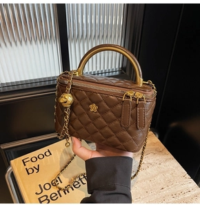Detail einer braunen gesteppten Box-Tasche mit Goldgriff und Kettenriemen