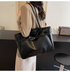 Detail shot of a black PU leather tote bag worn by a model in a minimalist room