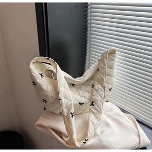 Detail of cream quilted tote bag with black bow embroidery and smooth zipper closure