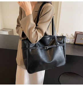 Detail of minimalist black PU leather tote bag with decorative buckle strap and twin handles