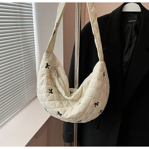 Close-up of cream quilted puffer bag with black bow embroidery and silver zipper detail