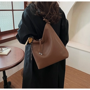 Dettaglio di borsa a spalla in pelle marrone con nappe a coulisse e ciondolo a sfera