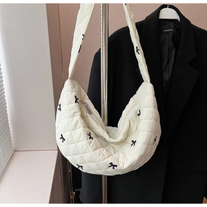 Close-up of beige quilted crescent bag featuring black bow embroidery and rhombic stitching