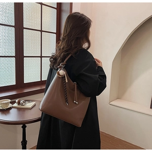Dettaglio della borsa tote in pelle marrone scuro con ciondolo da baseball sulla tracolla