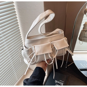Detail shot of a white glossy faux leather baguette bag with bow straps and pockets