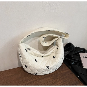 Detailed close-up of a white quilted crescent bag featuring small black bow embroidery
