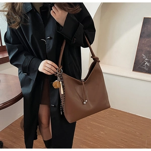 Dettaglio di una borsa tote marrone con tracolla a nodo e chiusura a coulisse decorata
