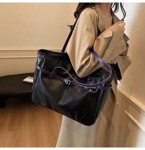Close-up of black tote bag featuring purple straps and metallic silver buckles