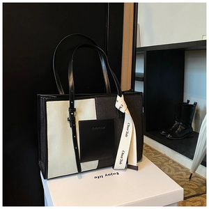 Detail of a color-block denim tote bag with leather front pocket and silk ribbon
