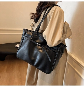 Detailed close-up of a black leather tote bag with metal buckles on a woman shoulder