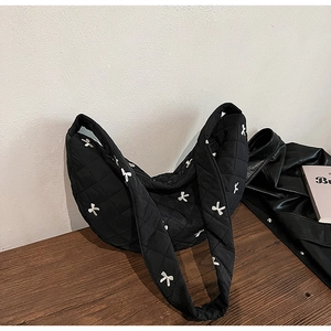 Detail of black quilted shoulder bag with white bow patterns and soft moon-shaped design