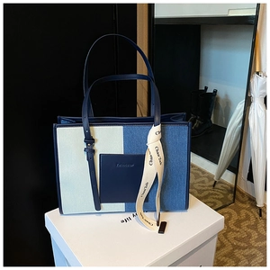 Detail of color-block denim tote bag with navy leather pocket and decorative ribbon