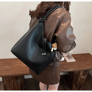 Dettaglio borsa tote in pelle nera con tracolla a nodo e ciondolo a forma di fungo peluche