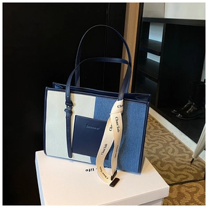 Detail of blue and beige canvas tote bag with leather pocket and decorative ribbon strap