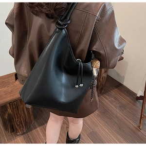 Dettaglio borsa hobo in pelle nera con tracolla a nodo e ciondolo a fungo in legno