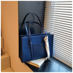 Detail of dark blue denim tote bag featuring a leather pocket and decorative ribbon