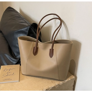Detail of a khaki leather tote bag featuring dark brown straps in a minimalist setting