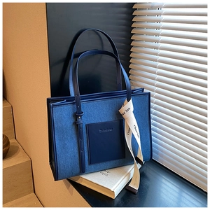 Detail of a dark blue denim tote bag with leather handles on a sunlit windowsill