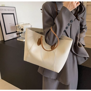 Side view of a cream tote bag with brown handles worn by a model in a grey suit