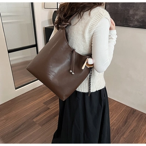 Dettaglio della borsa hobo marrone scuro con tracolla annodata e ciondolo da baseball