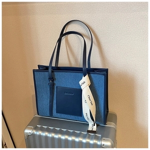 Detailed close-up of dark denim tote bag with leather straps and branded ribbon accent