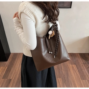 Dettaglio borsa tote in pelle marrone con manico intrecciato e ciondolo da baseball