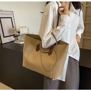 Detail of minimalist khaki tote bag featuring contrasting dark brown leather handles