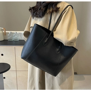 Detail of a black large capacity leather tote bag worn with a stylish khaki trench coat
