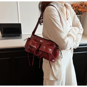Detail of burgundy patent leather baguette bag with bow drawstring and multiple pockets
