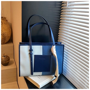 Detailed close-up of blue denim patchwork tote bag with leather logo and ribbon decor