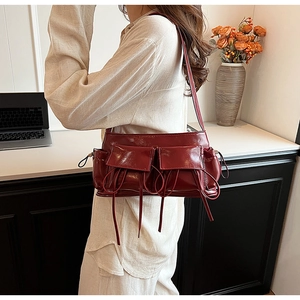 Detail of burgundy glossy baguette bag with bow drawstrings and utility pockets