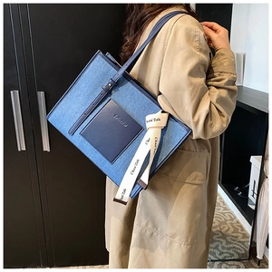 Detail of denim tote bag with leather pocket, logo embossing and letter print ribbon