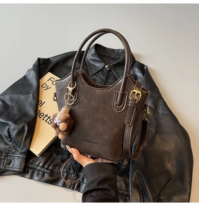 Dettaglio borsa a secchiello vintage marrone con ciondolo a orsetto e tracolla con fibbia oro