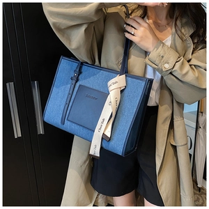 Detail of denim tote bag with leather trim and silk ribbon on camel trench coat